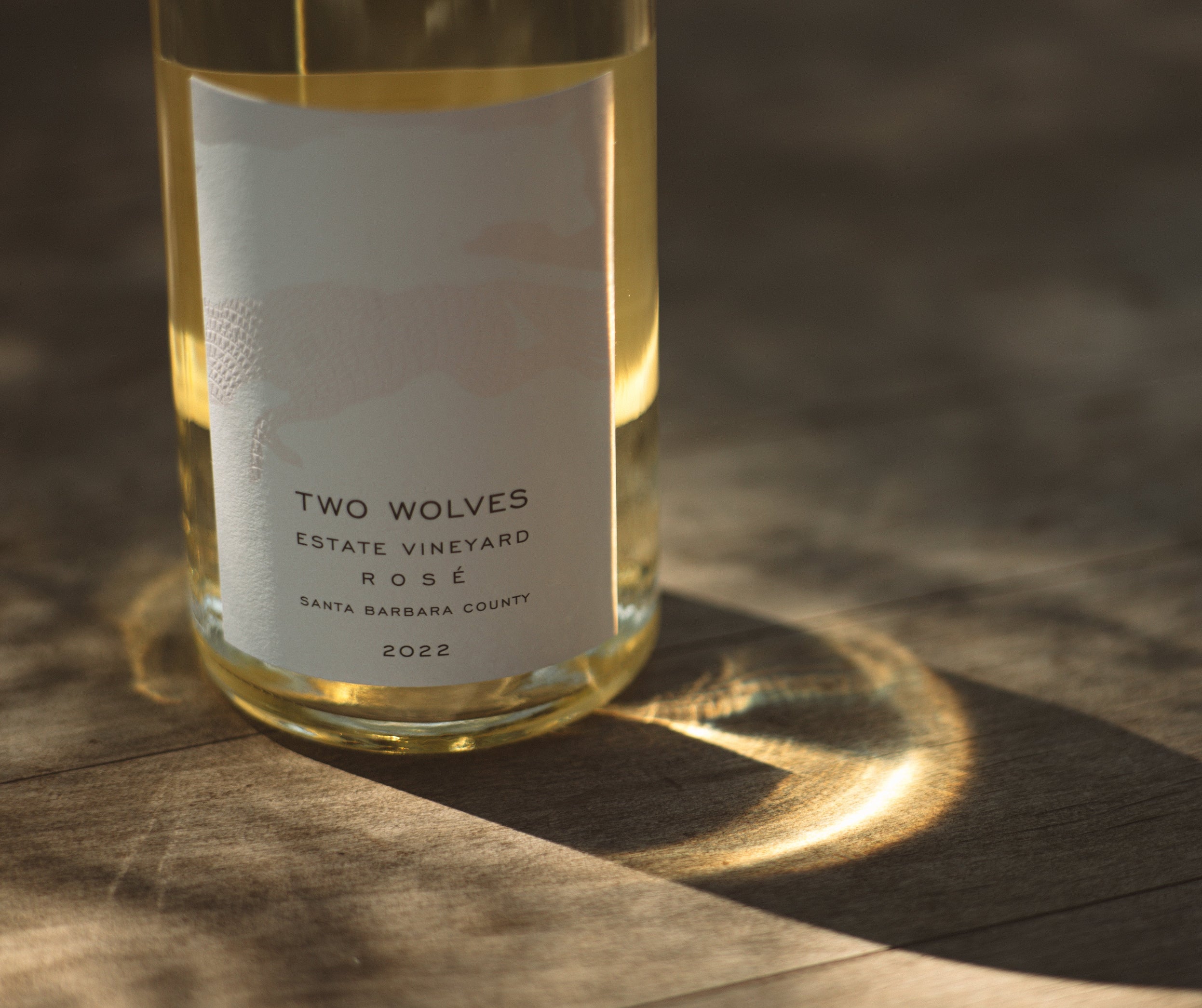 Two Wolves Rosé bottle on table with sunlight shining through.